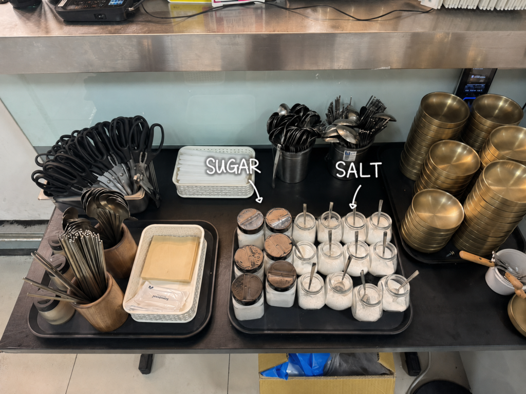 The self-serve station at a kongguksu restaurant, with jars of sugar on one tray and jars of salt on the next.