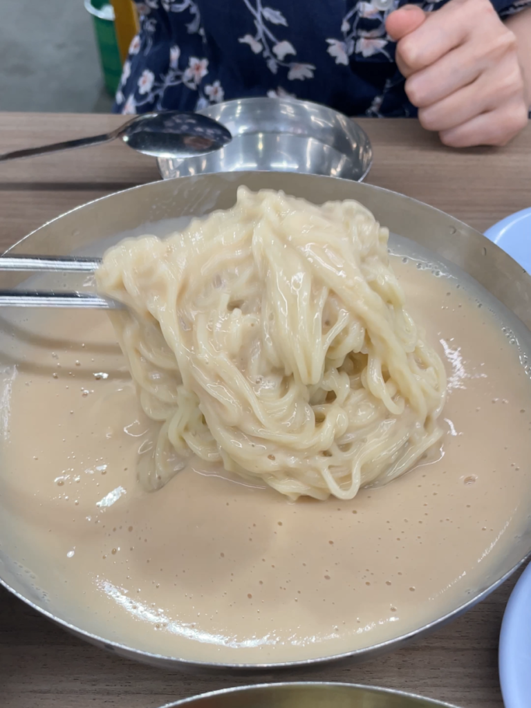 Kongguksu in a steel bowl, the noodles lifted clear of the thick white soybean broth with chopsticks.