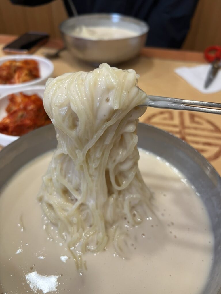 Noodles lifted out of the bean broth with chopsticks, coated in the thick white soup.