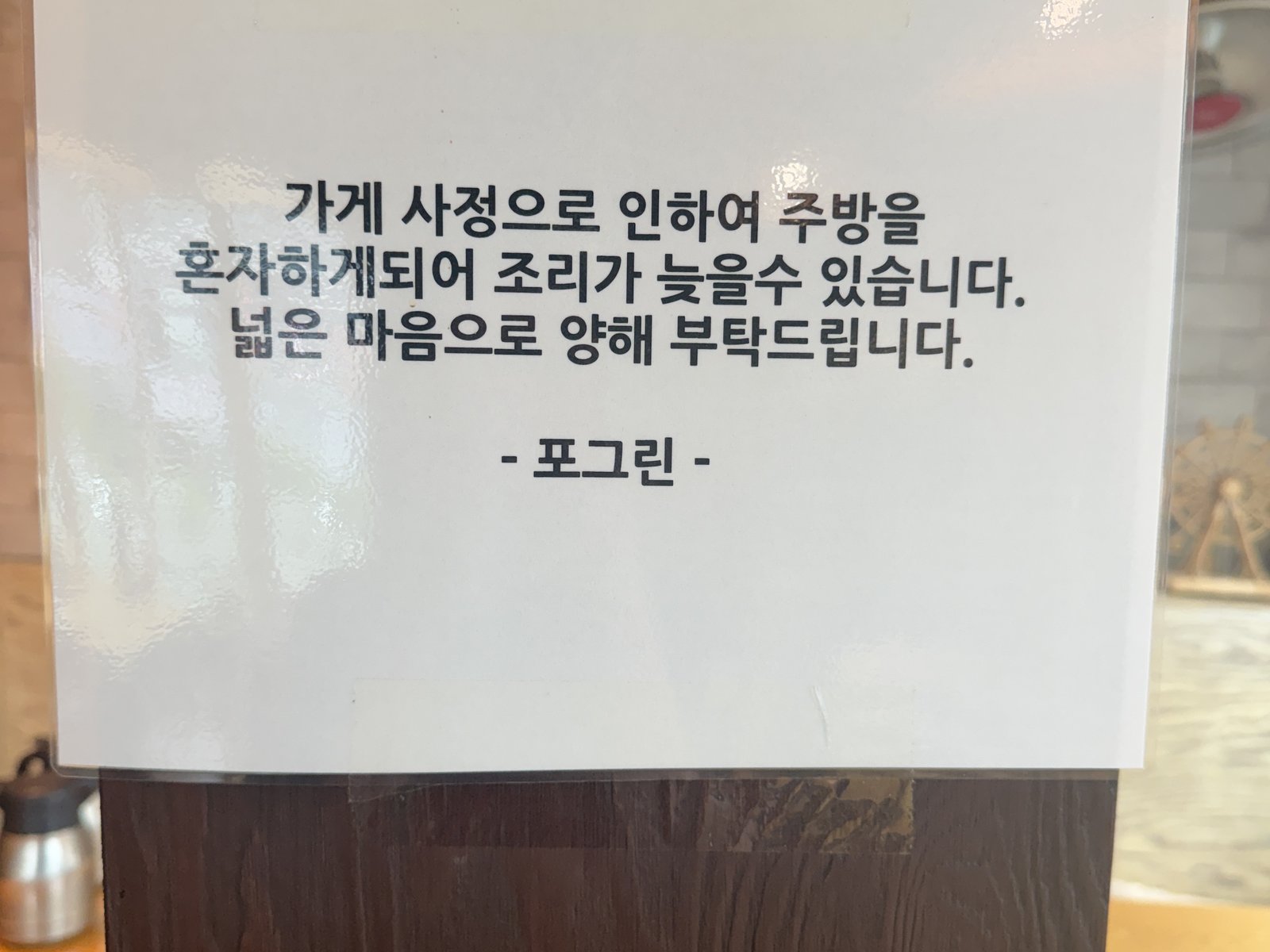 A printed notice taped to a wooden post: one person is working the kitchen today, so the food may be slow.