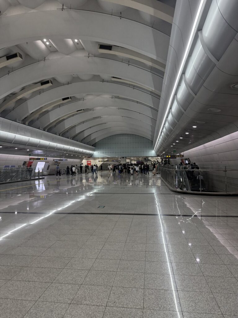 A wide underground station concourse in Seoul at rush hour, commuters walking toward the escalators.